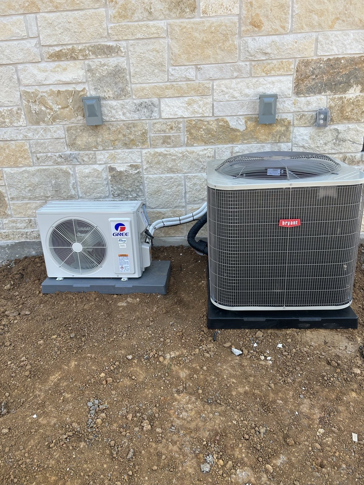 Outdoor HVAC condenser and mini-split equipment set beside a stone exterior wall.