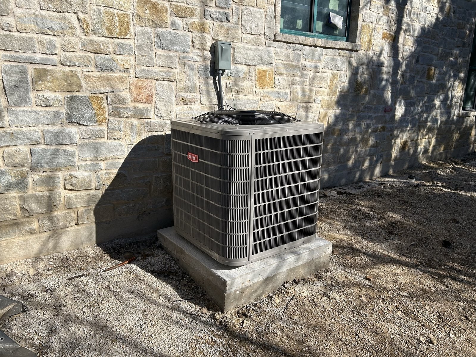 Outdoor HVAC condenser installed on a concrete pad beside a stone wall.