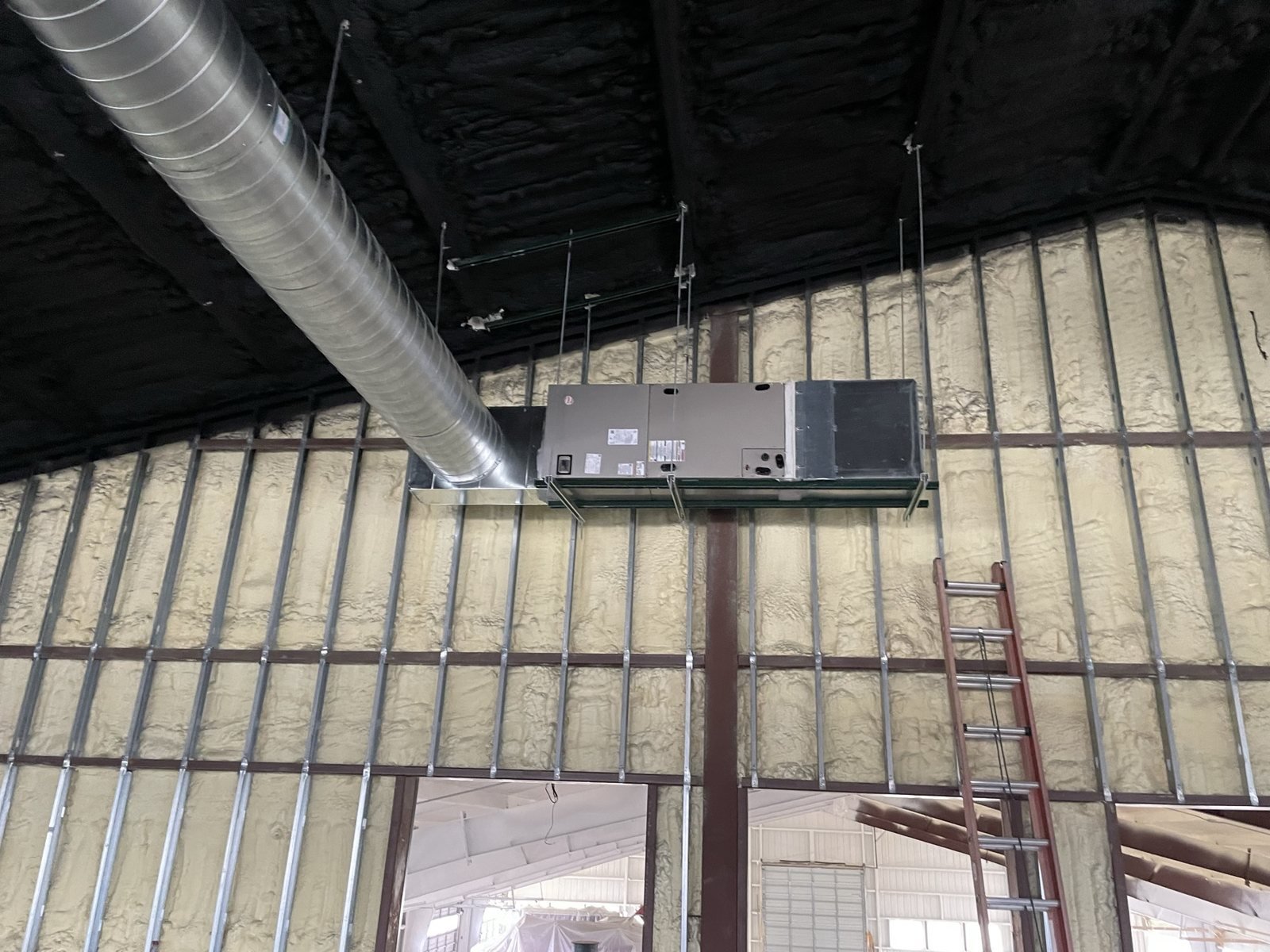 Large interior HVAC equipment with ductwork in an insulated metal building.