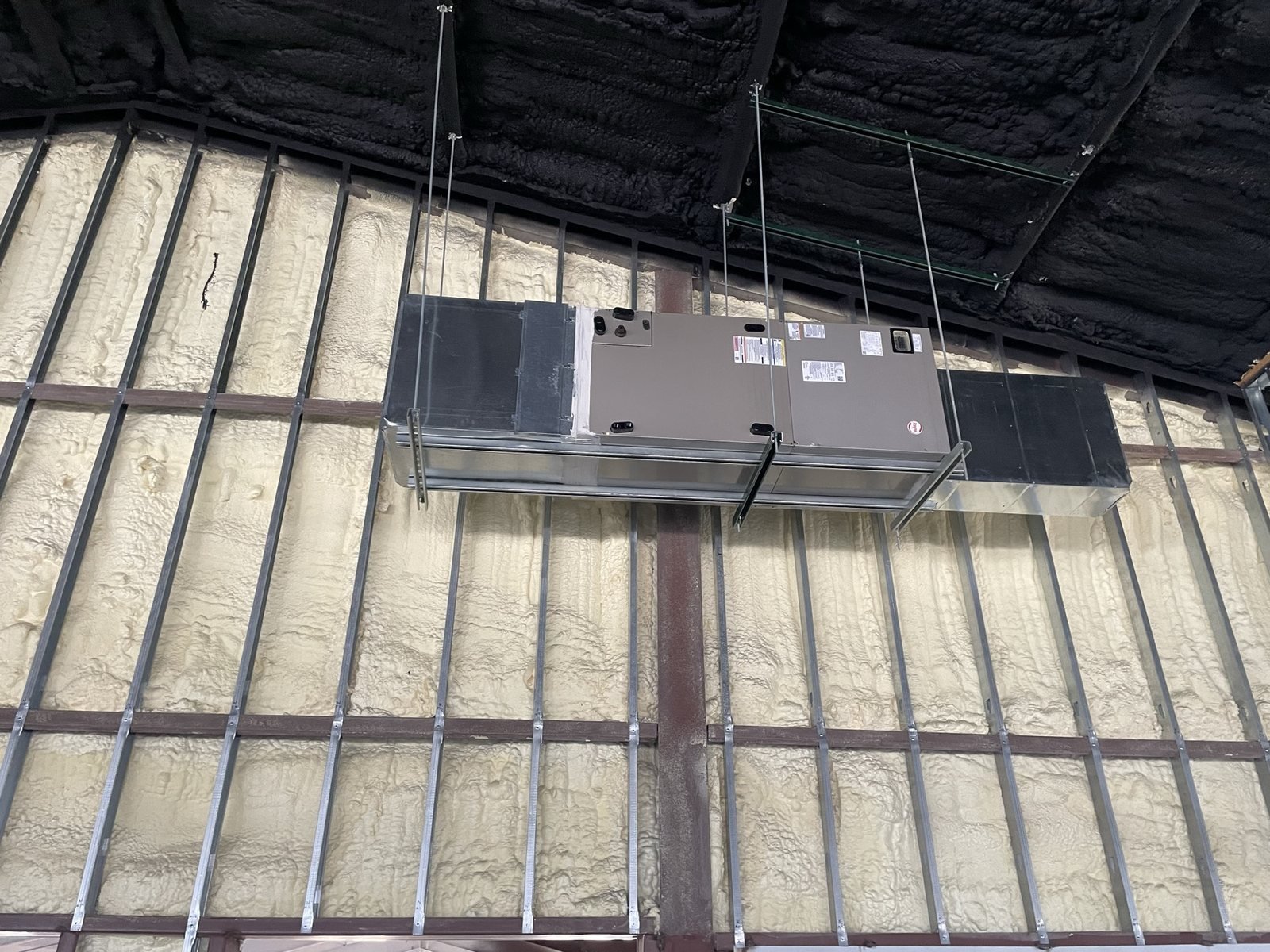 Ceiling-suspended HVAC equipment connected to ductwork in a metal building.