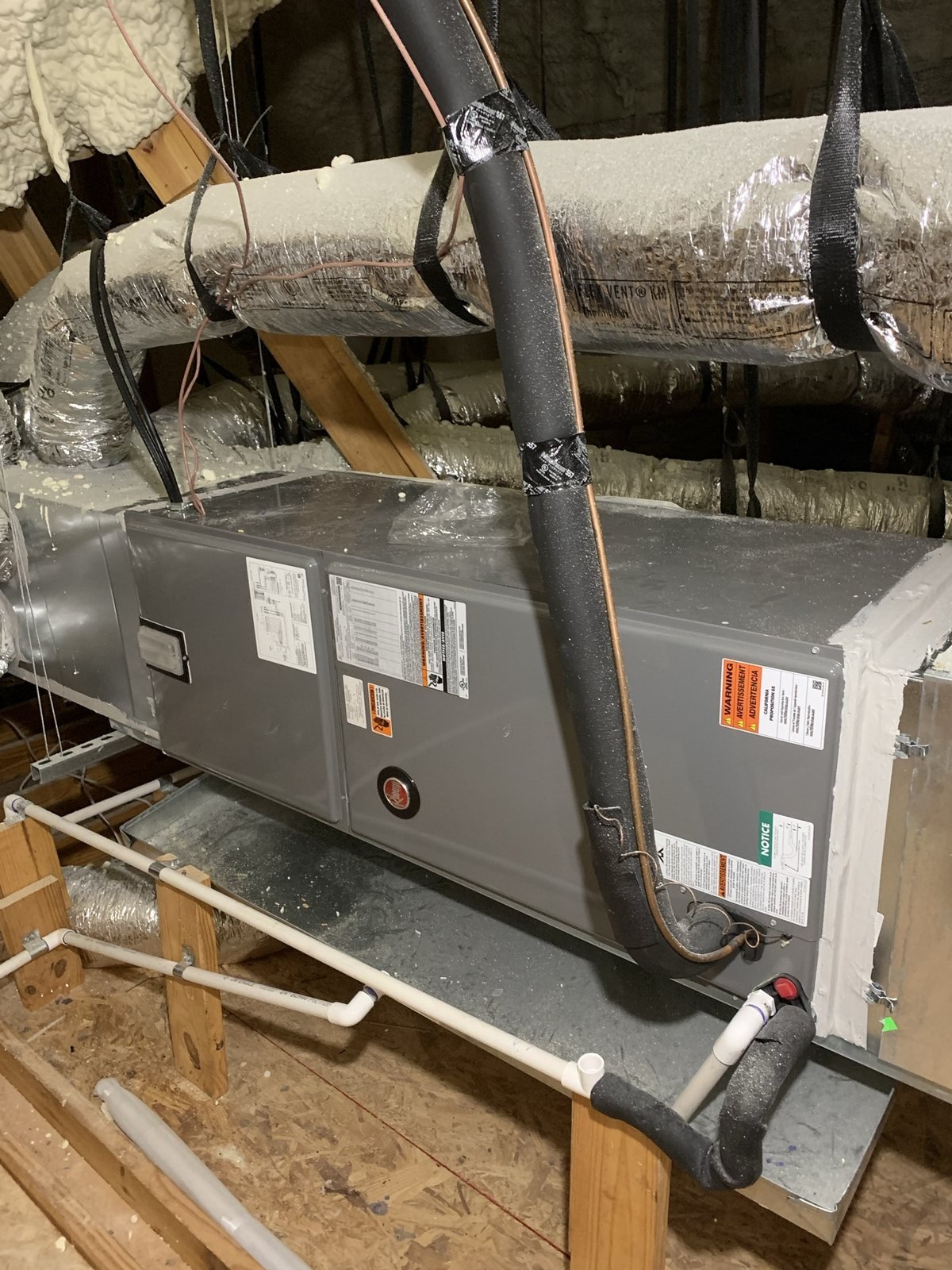 Attic HVAC air handler with duct, drain, and line connections.